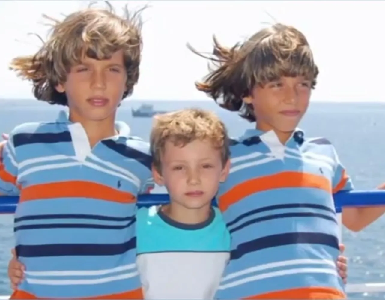 The twins as children in matching striped polo shirts on a boat, with their little sister Alba between them