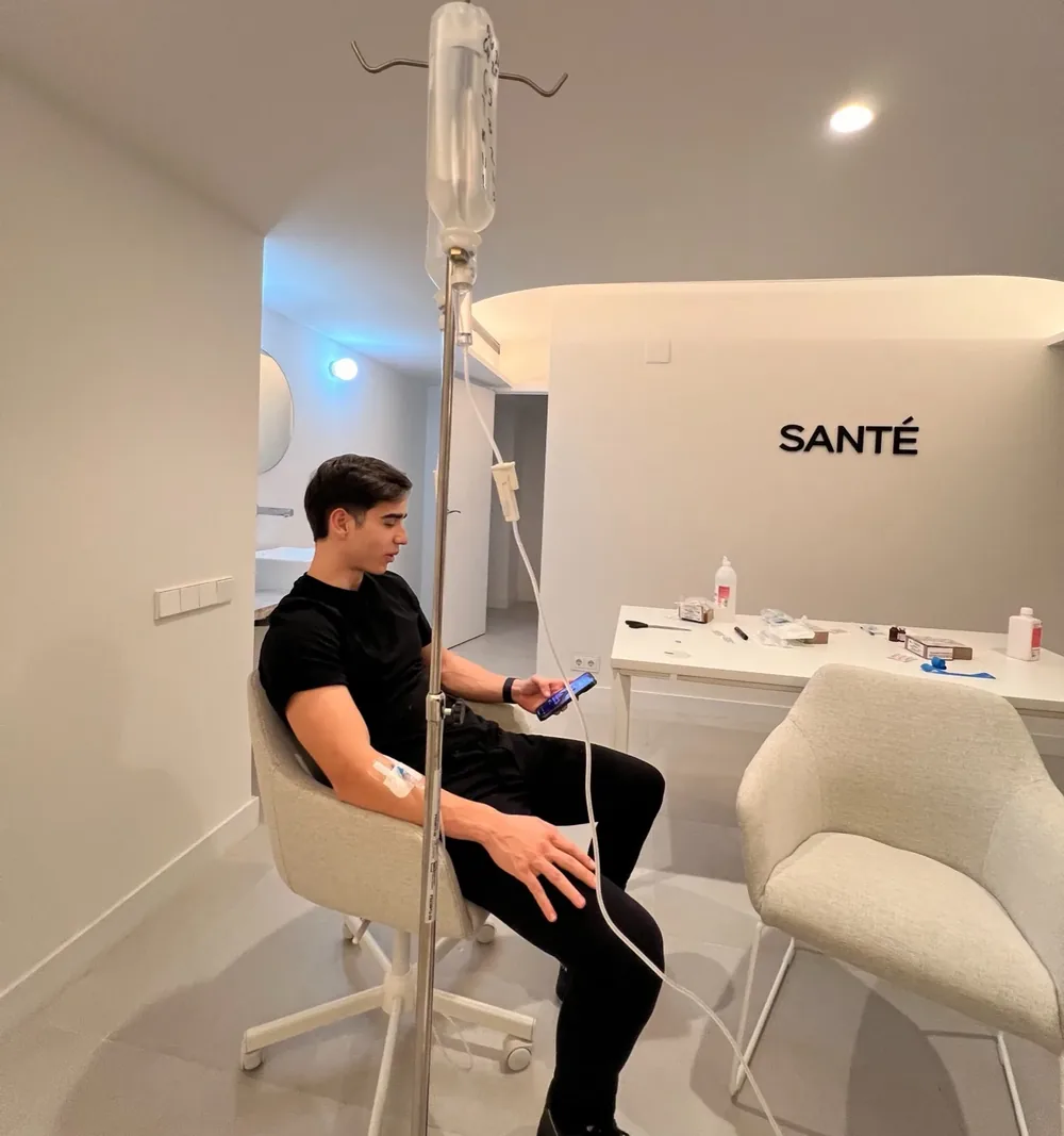 One of the twins on an IV drip in a white Santé clinic room, looking at his phone