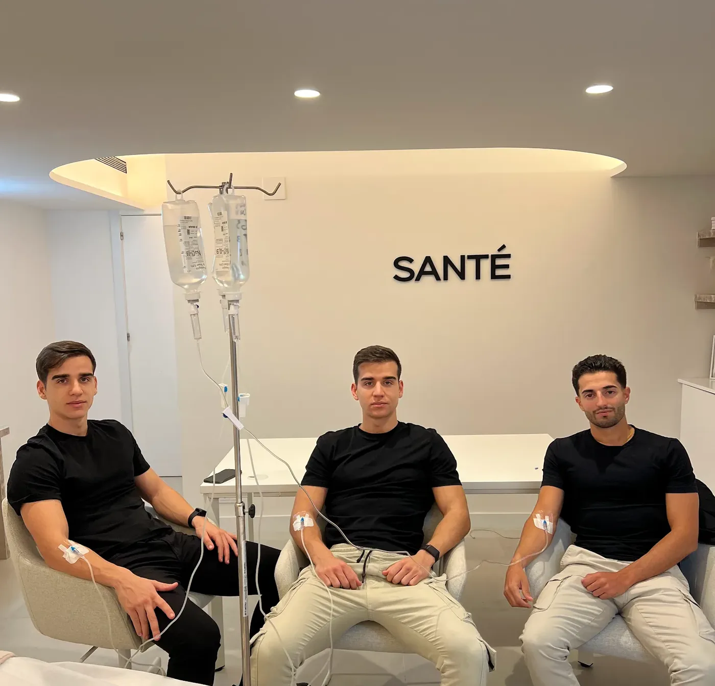 Three men in black sitting on IV drips in a white Santé clinic room
