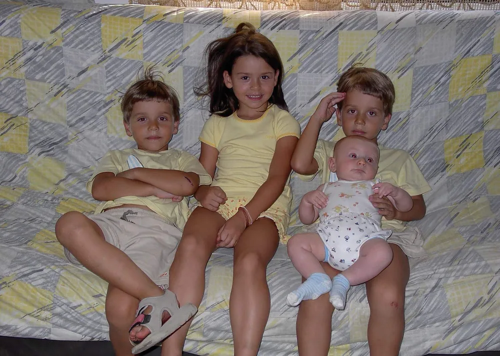 Four children sitting together on a sofa, the twins, a sister, and a baby