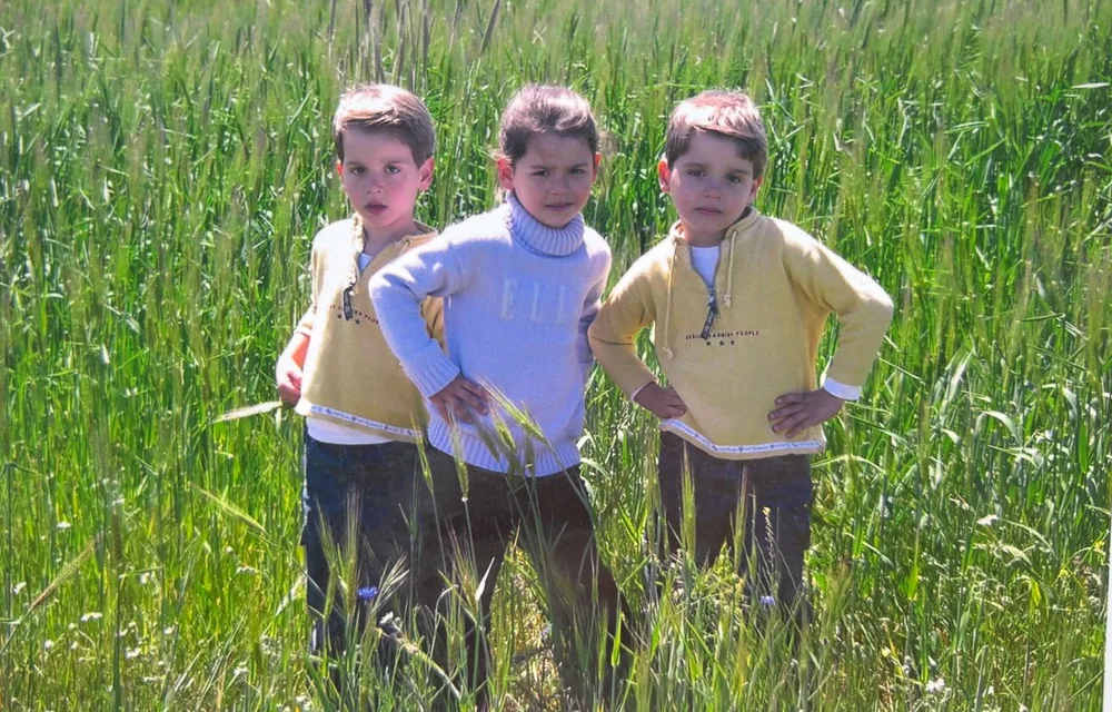 The twins and a sibling in matching polo shirts in tall green grass